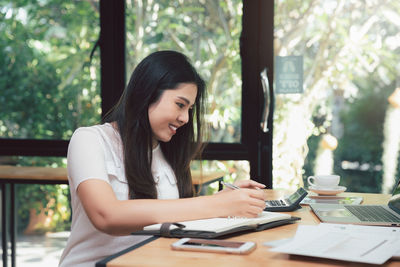 Young woman using mobile phone while sitting on table