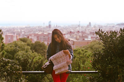 Woman reading map against sky