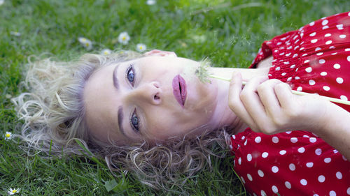 Portrait of woman blowing flower while lying in park