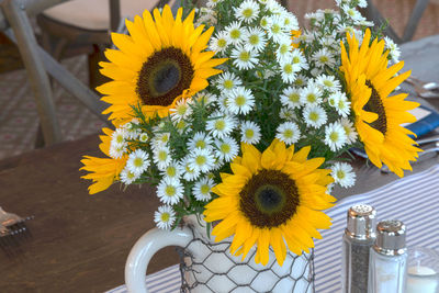 Fresh yellow sunflowers and white daisies bloom in a white vase covered with chicken wire