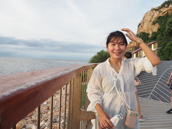 Portrait of smiling woman standing on railing against sea