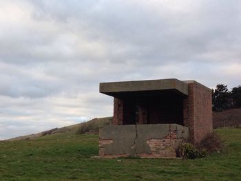 Built structure on grassy field against cloudy sky