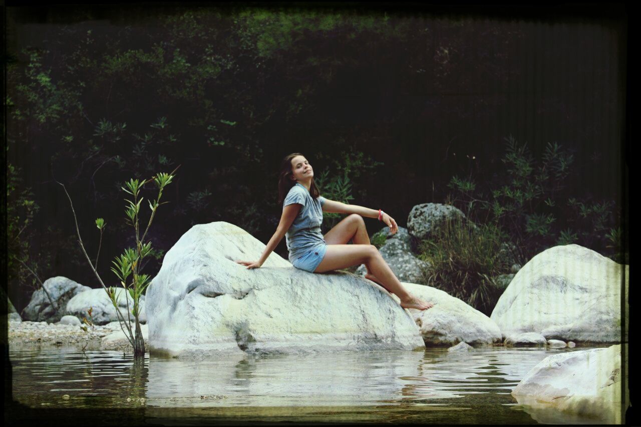 water, lifestyles, leisure activity, full length, person, young adult, waterfront, sitting, lake, casual clothing, holding, rock - object, young men, front view, reflection, three quarter length, side view