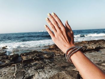 Cropped hand of woman gesturing at beach against sky