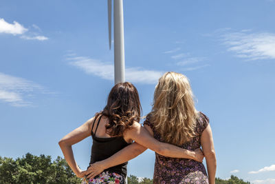 Two beautiful women travelers while taking pictures with a wind turbine in the background