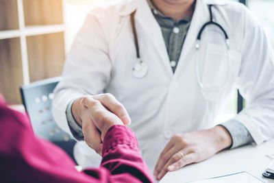 Midsection of patient handshaking with doctor at hospital