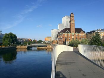 Bridge over river by buildings against blue sky