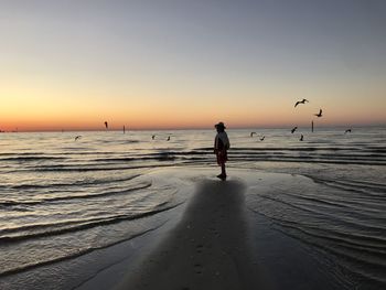 Silhouette woman standing at beach against clear sky during sunset