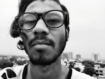 Close-up portrait of serious young man wearing eyeglasses against clear sky