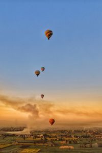 Hot air balloons flying over landscape against sky during sunset