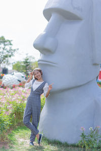 Full length portrait of young woman pointing while standing by statue