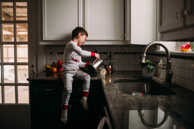 Young boy pouring flothed milk into cup of coffee on kitchen counter