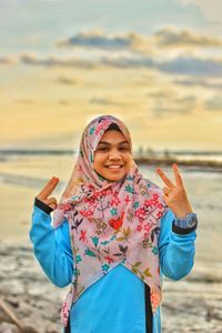 Portrait of smiling young woman using phone while standing on beach