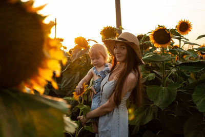 Beautiful mother holds a little son in her arms in a field of sunflowers at sunset