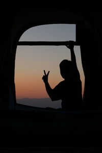 Silhouette man standing by window at sunset