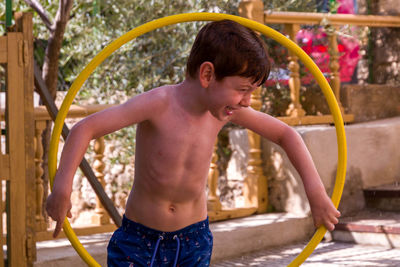 Shirtless boy standing outdoors playing with ring