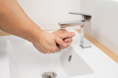Men's hands under a stream of water in the washbasin