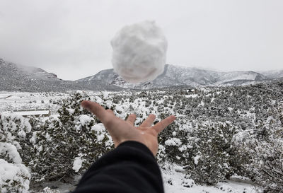 Cropped hand playing with snowball against mountains