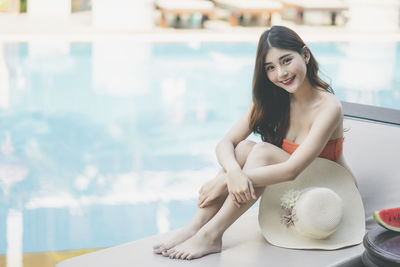 Portrait of a smiling young woman sitting on lounge chair by swimming pool