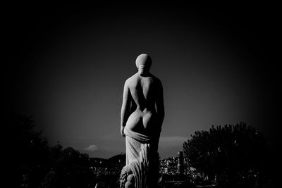 Rear view of statue against trees against clear sky