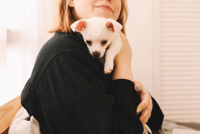 A happy teenage girl is playing kissing having fun with her pet a small dog in a bed in a cozy house