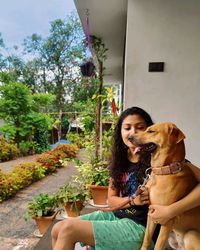 Woman with dog sitting against plants