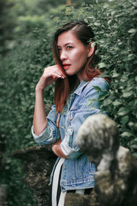 Young woman looking away while standing against tree