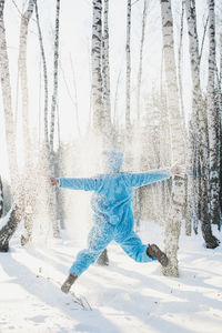 Rear view of mid adult man jumping on snow covered field in forest