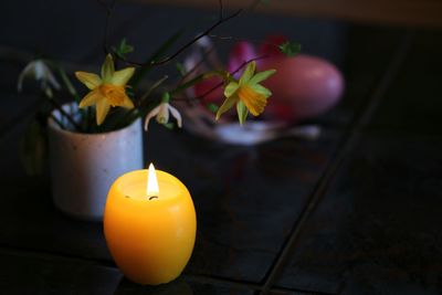 Lit candle by daffodils in cup on table