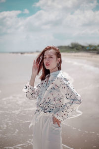 Young woman standing at beach against sky