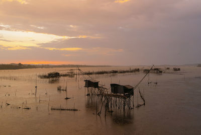 Wooden posts in sea against sky at sunset