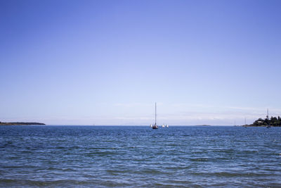 Sailboat in sea against clear blue sky