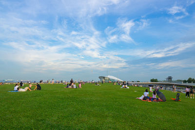 People relaxing on field against sky