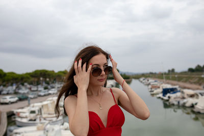 Woman wearing sunglasses while standing against boats moored at harbor