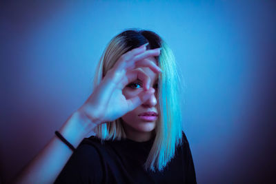 Portrait of beautiful woman looking through hand against wall