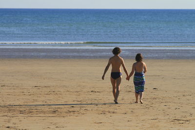 Rear view of siblings walking on beach