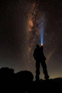 Rear view of silhouette man holding flashlight against star field