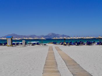 Deck chairs on beach against clear blue sky