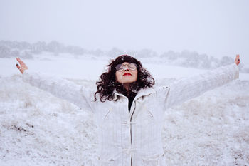 Young woman with arms outstretched standing on field during snowfall