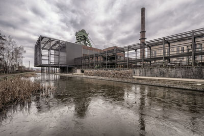 Factory by river against sky