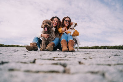 Female friends with dogs sitting on footpath