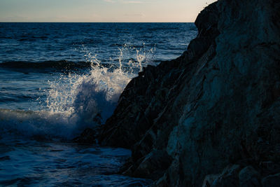 Waves splashing on rocks at shore against sky