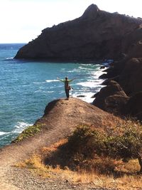 Man standing on rock by sea against sky