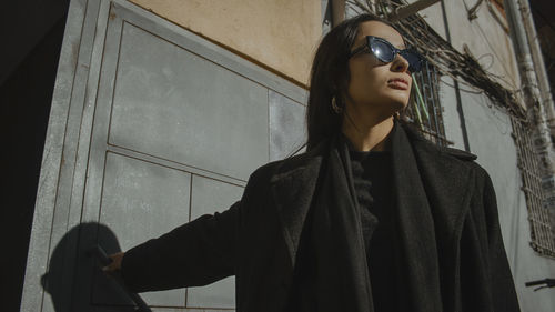 Young woman looking away while standing against wall