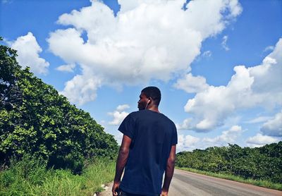 Rear view of man standing by trees against sky