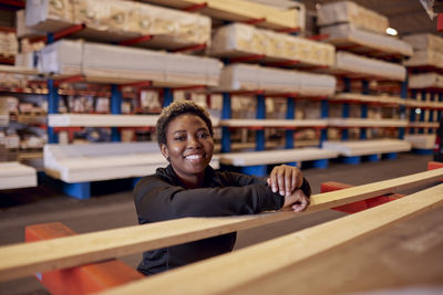 Portrait of smiling female worker leaning on plank in lumber industry