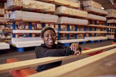 Portrait of smiling female worker leaning on plank in lumber industry