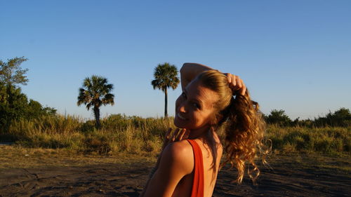 Portrait of young woman standing on sand against clear blue sky