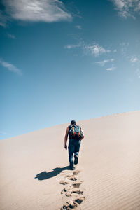 Woman walking on sand dune in desert against sky