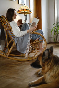 Young woman reading book with dog german shepherd, sitting on rocking chair. cozy home atmosphere